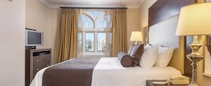 A hotel room with a bed, a desk with a computer, a telephone, and a window with curtains.