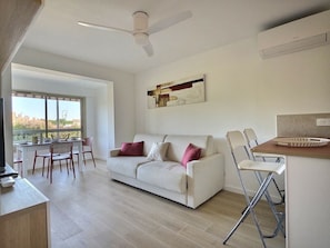 Ein modernes Wohnzimmer mit einer Couch, Sesseln, einem Esstisch und einem großen Fenster.