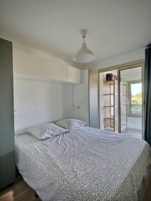 Ein Schlafzimmer mit Bett, Deckenleuchte, Kleiderschrank und einer Schiebetür zu einem Außenbereich.