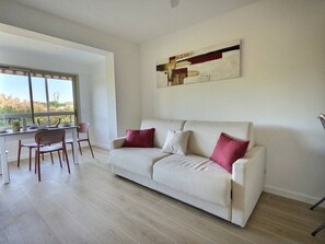 Ein modernes Wohnzimmer mit einer Couch, zwei Sesseln, einem Esstisch und einem großen Fenster.