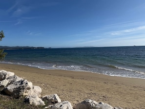 Una playa con cielo despejado, mar tranquilo y primer plano rocoso.