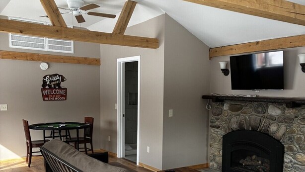 Una sala de estar tipo loft con vigas de madera a la vista, chimenea, televisor y mesa de billar.
