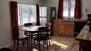 Una cocina moderna con comedor, armarios de madera, refrigerador empotrado y una ventana con cortinas.