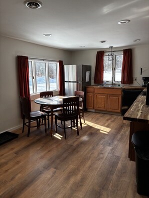 A modern kitchen with a dining area, wooden cabinets, a built-in refrigerator, and a window with curtains. - Killington / Rutland   2 Bdrm Cabin w/ Mtn view (Mendon)