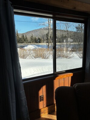 A cabin interior with a large window, wooden walls, and a view of a snowy landscape. - Killington / Rutland   2 Bdrm Cabin w/ Mtn view (Mendon)