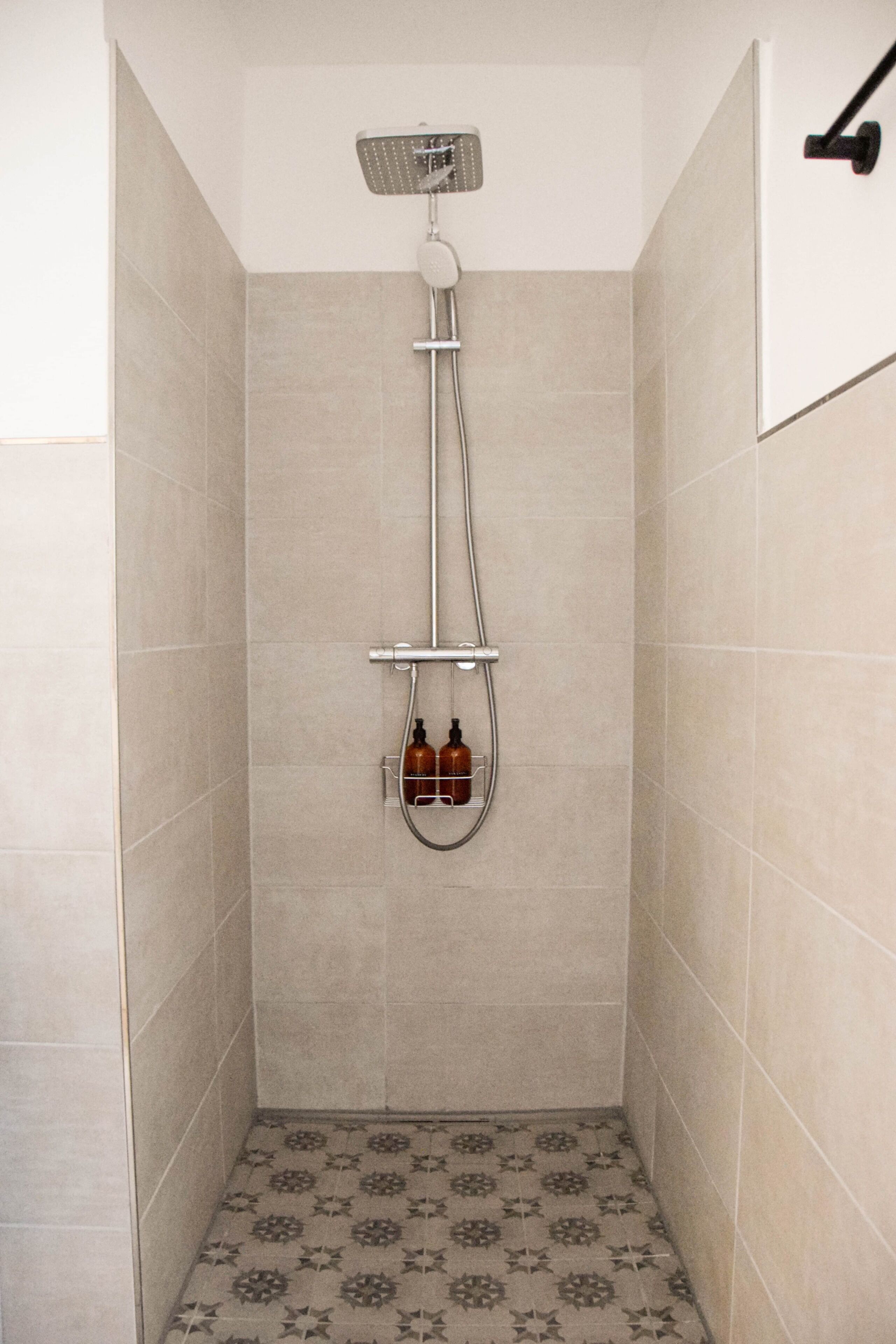 A shower with a handheld showerhead, a wall-mounted faucet, and two bottles of shampoo.