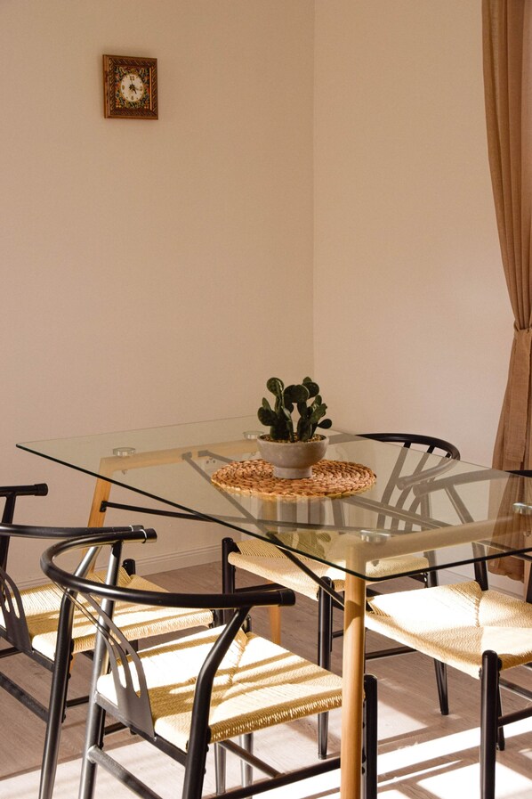 Un coin repas avec une table en verre, des chaises en osier, une plante succulente et une horloge au mur.