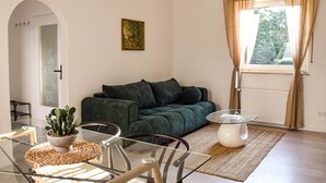 Un salon avec un canapé vert, une table basse en verre, une plante en pot et un tableau accroché au mur.