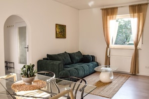 Ein Wohnzimmer mit einem grünen Sofa, einem Glastisch, einer Topfpflanze und einem Bild an der Wand.