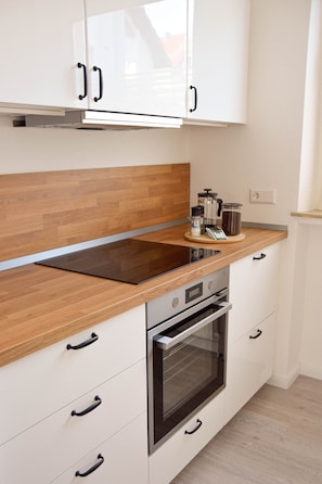 A modern kitchen with white cabinets, a wooden countertop, a built-in oven, and a coffee maker.