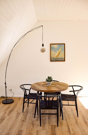 Een ronde houten tafel met vier stoelen, een bloempot, een vloerlamp en een lijst met een schilderij aan de muur.