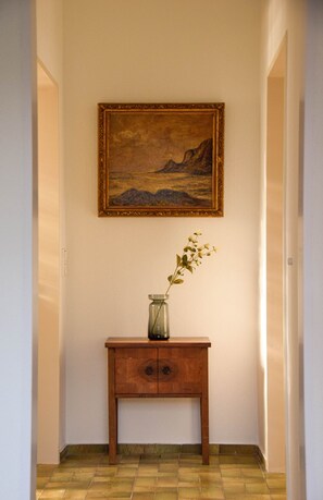 Een hal met een houten console tafel, een vaas met een plant en een lijst met een schilderij aan de muur.