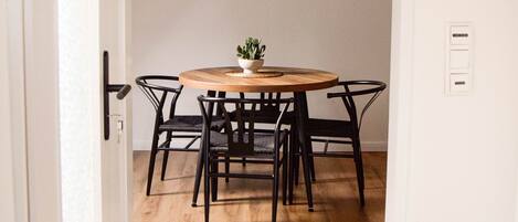 A dining area with a round table, black chairs, a hanging light fixture, and a sailboat painting on the wall.