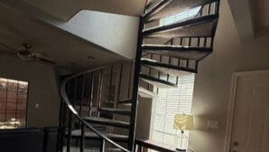Uma escada em espiral com corrimão de metal, um ventilador de teto e uma janela com persianas.
