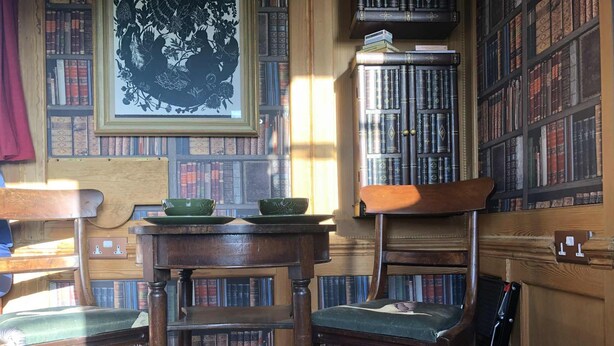 Ett bibliotek med trämöbler, bokhyllor och en inramad botanisk tavla.
