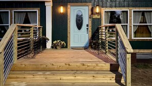A wooden building with a light blue door, a wooden deck, and a staircase leading to the entrance. - Soul Sanctuary and Happiness Tree (McDade)