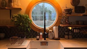 A kitchen with a round window, a sink, and a ceiling with intricate patterns. - Soul Sanctuary and Happiness Tree (McDade)