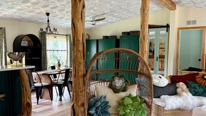 A room with a dining area, a wicker chair with cushions, a green ottoman, and a ceiling with a decorative pattern. - Soul Sanctuary and Happiness Tree (McDade)
