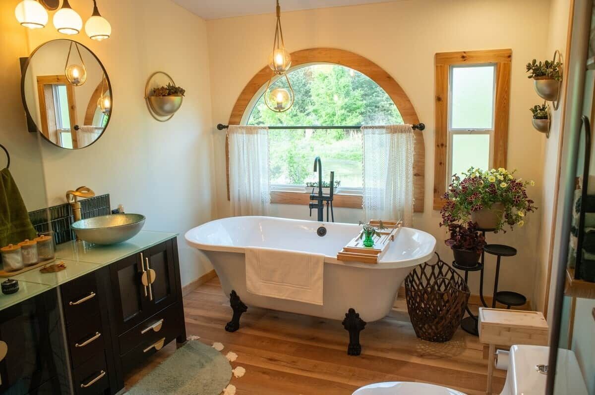 Une salle de bain avec une baignoire sur pieds, un grand miroir, une fenêtre avec des rideaux et une plante en pot.