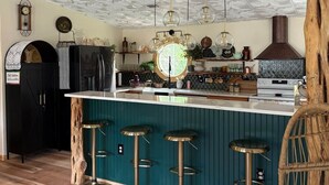 A kitchen with a central island, bar stools, a hanging light fixture, and a clock on the wall. - Soul Sanctuary and Happiness Tree (McDade)