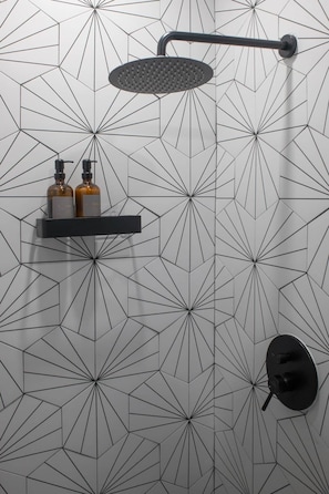 A bathroom with a geometric patterned wall, a showerhead, and a shelf with two bottles.