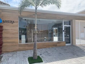 Un edificio moderno con fachada de madera, entrada de cristal y una palmera frente a él.