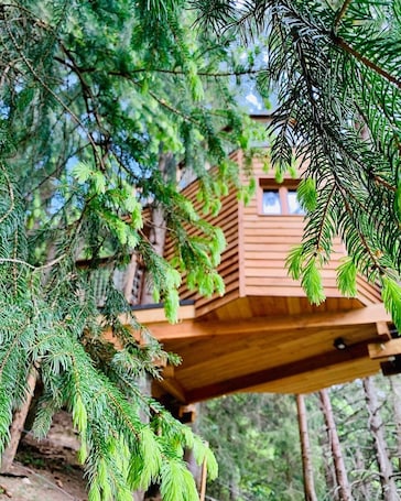 A wooden treehouse elevated among dense green foliage.. Valmo Insolite tree house