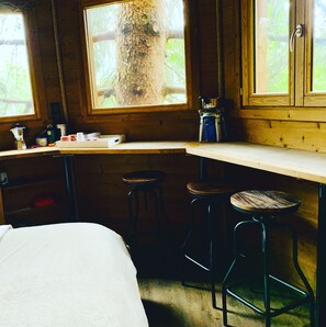 A cabin interior with a bed, a desk, two stools, and a window overlooking a tree. - Valmo Insolite tree house (Les Avanchers-Valmorel)