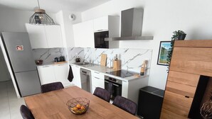 A modern kitchen with white cabinets, a marble backsplash, a dining table with purple chairs, and a wooden cabinet with a plant. - Luxury, modern, and cozy apartment just 5 minutes from the Baillargues Golf Course  (Baillargues)