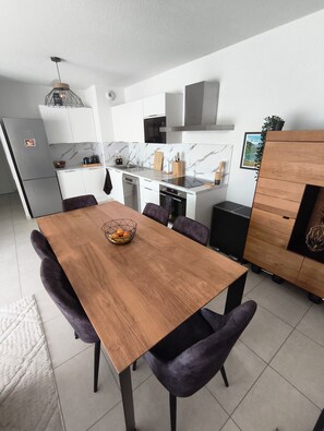 Eine moderne Küche mit weißen Schränken, einer Marmor-Spritzschutzleiste, einem Esstisch mit violetten Stühlen und einem Holzschrank mit einer Pflanze.