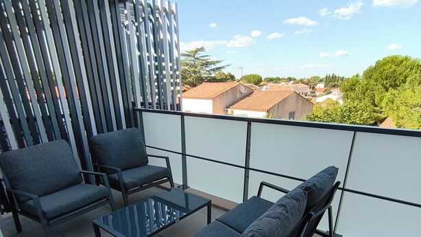 A balcony with a view of buildings and trees, featuring a sofa, chairs, and a small table. - Luxury, modern, and cozy apartment just 5 minutes from the Baillargues Golf Course  (Baillargues)