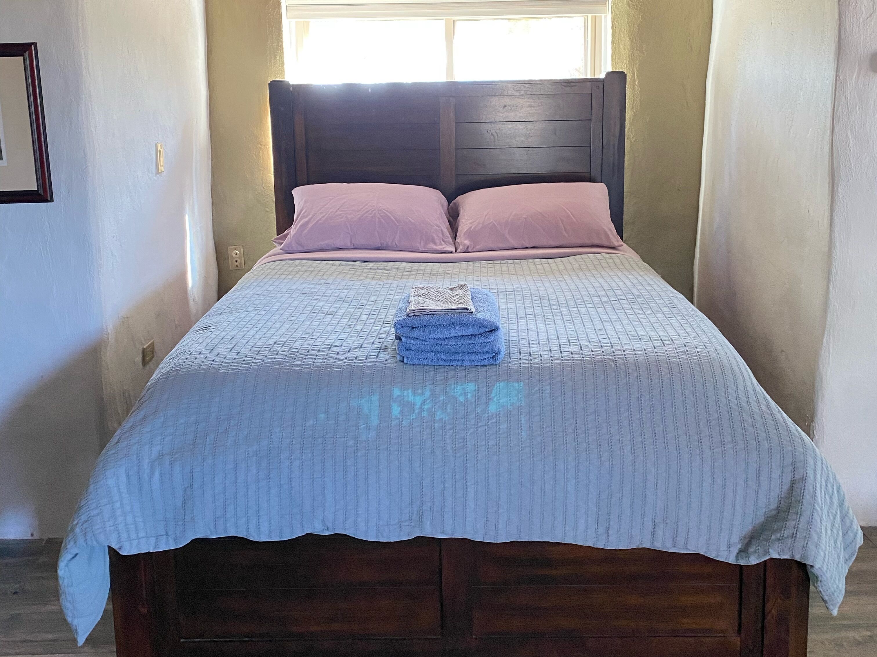 Una cama con cabecera de madera, una toalla azul doblada y dos almohadas rosas.