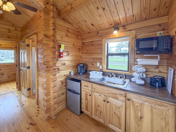 A wooden cabin kitchen with a refrigerator, sink, microwave, and coffee maker.