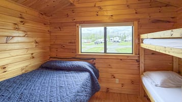 Une cabane avec un lit superposé, une fenêtre donnant sur un terrain de camping et des murs en bois.