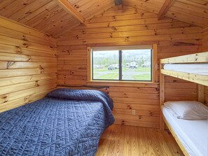 Une cabane avec un lit superposé, une fenêtre donnant sur un terrain de camping et des murs en bois.