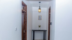 Un couloir aux murs blancs, une console noire surmontée d’un vase et des portes en bois.