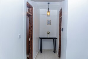 A hallway with white walls, a black console table with a vase, and wooden doors. - Shanvinhomes - 2 Bedroom Apartment in Elgonview near Reale Hospital (Eldoret)