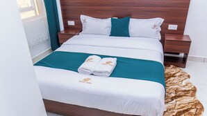Un lit bien fait, avec du linge de lit blanc et des touches de couleur turquoise, une tête de lit en bois, une petite table de chevet et un tapis à motifs.