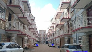 Un immeuble résidentiel à plusieurs étages, doté de balcons, d’une cour intérieure et de voitures garées.