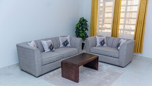 Un salon avec deux canapés gris, une table basse en bois, une plante en pot et des rideaux jaunes.