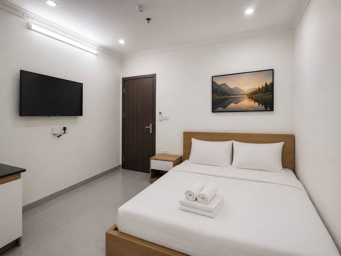 A hotel room with a bed, a TV, a painting, and a door.