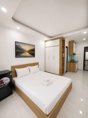 A modern bedroom with a bed, a wardrobe, a small kitchenette, and a painting on the wall. - Dreamora Serenity Hotel & Residence (Ba Dinh)