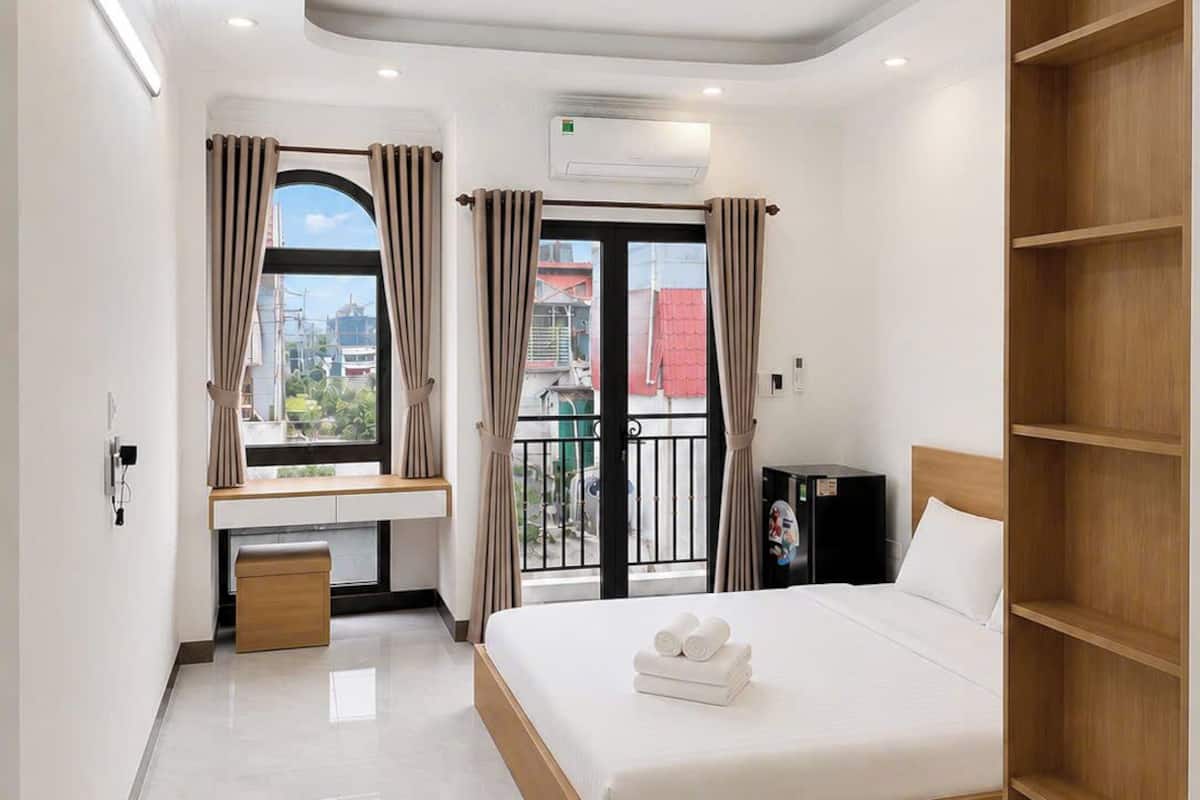 Une chambre d’hôtel moderne équipée d’un lit, d’un bureau, d’une armoire et d’un balcon avec des rideaux.