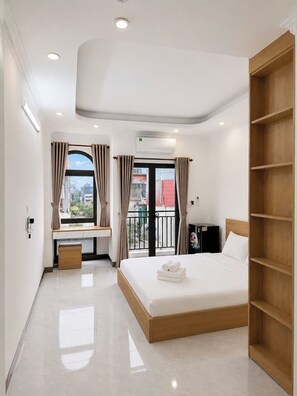 Habitació d'hotel moderna amb un llit, escriptori, armari i un balcó amb cortines.