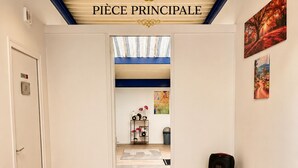 Käytävällä on kyltti, jossa lukee ”PIÈCE PRINCIPALE”, ja se johtaa huoneeseen, jossa on JBL-kaiutin kolmijalkaisella jalustalla.