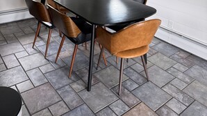 Un coin repas avec une table noire et des chaises marron, un luminaire suspendu et une fenêtre donnant sur un paysage verdoyant.