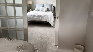 Une chambre à coucher comprenant un lit, une table de chevet, une lampe et une porte donnant sur une autre pièce.