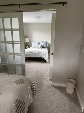 Een slaapkamer met een bed, nachtkastje, lamp en een deur naar een andere kamer.