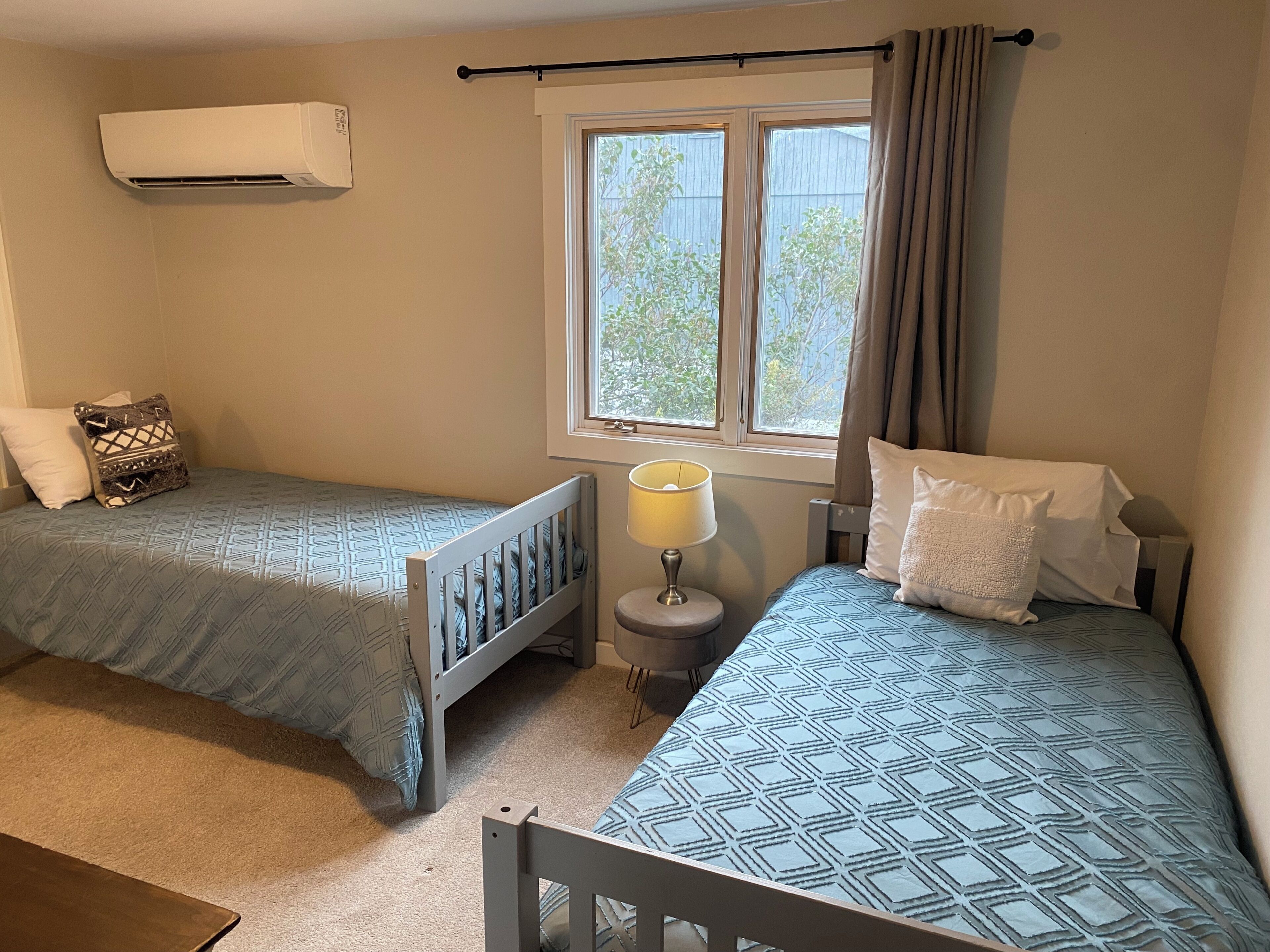 Quarto com duas camas de solteiro, janela com cortinas, ar condicionado e abajur.