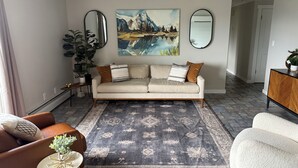 Un salon avec un canapé, une table basse et un tapis. Il y a un tableau au mur et une plante sur le côté.